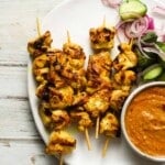 Grilled turmeric chicken skewers with sliced cucumbers, pickled onions, and dipping sauce.