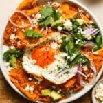 Plate of chilaquiles rojos topped with a fried egg, avocado, and cilantro.