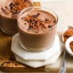 Two glasses of chocolate coffee milkshake topped with cocoa powder and chocolate chips.