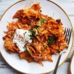 Pappardelle with mushroom ragu, topped with cream and herbs on a white plate.