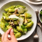 Green pesto pasta with tuna, garnished with shaved cheese and fresh basil leaves.