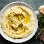 Creamy mashed potatoes with butter, rosemary, and garlic on a plate.