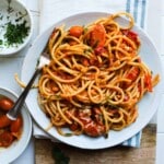 Plate of pasta with cherry tomatoes and herbs on a white plate.