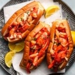 Three truffle butter lobster rolls garnished with chives, served with lemon wedges.