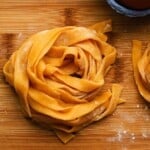 Freshly made pasta nests on a wooden board, sprinkled with flour.