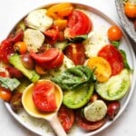 A colorful Caprese salad with tomatoes, mozzarella, basil, and dressing on a plate.