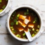 Bowl of miso broth with tofu and diced green onions on top.