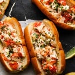 Lobster rolls topped with herbs and spices on a dark slate surface.