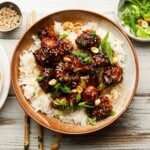 Bowl of kung pao crispy chicken with rice, topped with sesame seeds and peanuts.