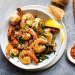Bowl of shrimp scampi garnished with herbs and lemon, served with bread.