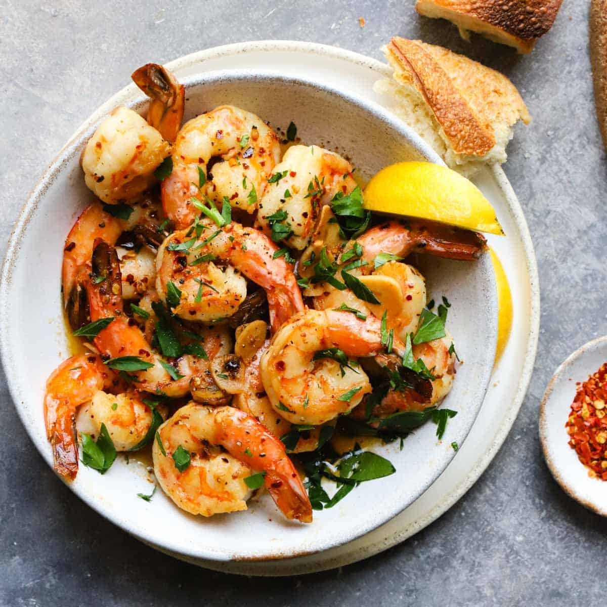 Bowl of shrimp scampi garnished with herbs and lemon, served with bread.