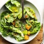 Green salad with herbs, croutons, and green goddess dressing in a white bowl.