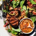 Grilled lamb chops with fresh herbs and spicy dipping sauce on a plate.