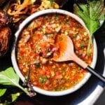 A bowl of vibrant, chunky salsa with a wooden spoon and fresh greens.