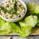 Bowl of tuna salad garnished with parsley, surrounded by fresh lettuce leaves.