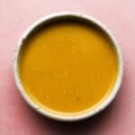 Bowl of creamy sesame mustard dressing on a pink surface.