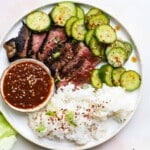 Grilled steak with white rice, cucumber slices, and a side of spicy sauce.