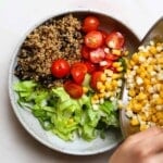 Bowl of quinoa, lettuce, cherry tomatoes, corn, and beans being prepared.