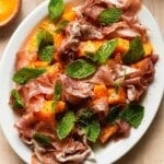 Plate of melon salad with prosciutto, fresh mint, and cracked black pepper.
