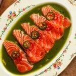 Sliced salmon topped with jalapeños served in basil oil on floral platter.