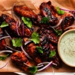 Grilled chicken wings with sambal sauce, garnished with onions and cilantro.