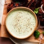 Bowl of creamy ranch garnished with herbs and accompanied by grilled wings.