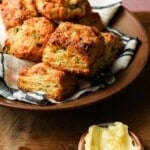 cheddar scallion biscuits stacked on a cloth-lined plate, served with butter.