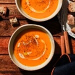 Two bowls of red kuri squash soup on a brown wooden table.