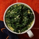 Creamed spinach with parmesan in a round cup on a red carpeted background.