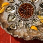 A plate of oysters over ice with lemon and mignonette in a bowl.