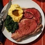 Prime rib, mashed potatoes, and creamed spinach on a plate with a fork and knife.