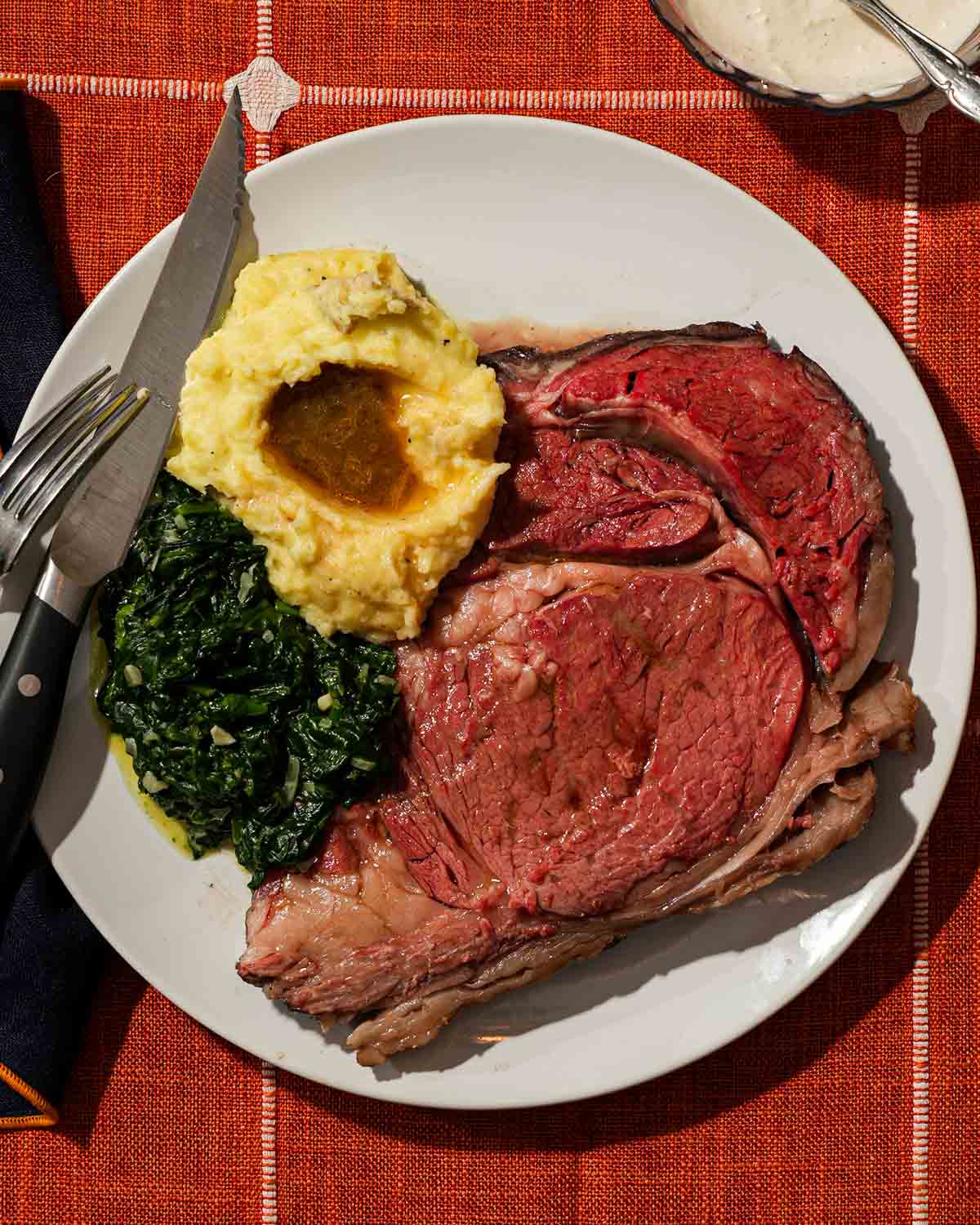 A plate with prime rib, mashed potatoes with gravy, and sautéed spinach on a tablecloth.