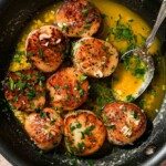 Seared scallops in a pan topped with chopped garlic and herbs in buttery sauce.