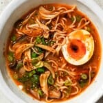 Bowl of spicy miso ramen with egg, scallions, mushrooms, and crispy garlic garnish.