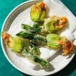 Fried stuffed squash blossoms on a white plate, seasoned with pepper.