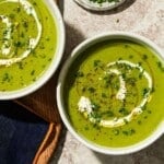 Two bowls of creamy green soup topped with chives and cream.