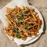 A plate of crispy fries topped with Parmesan cheese and herbs, served on parchment paper.