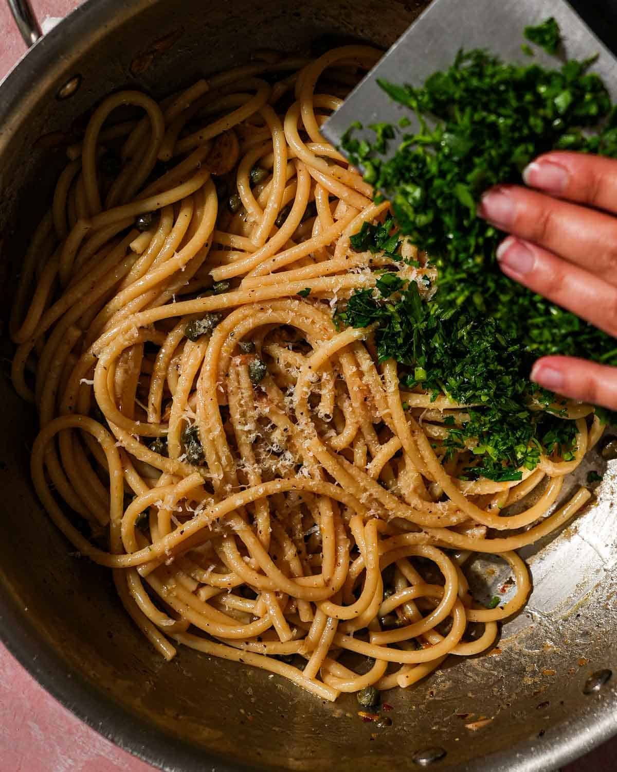 Adding freshly chopped parsley to pasta with capers and cheese in a pan.