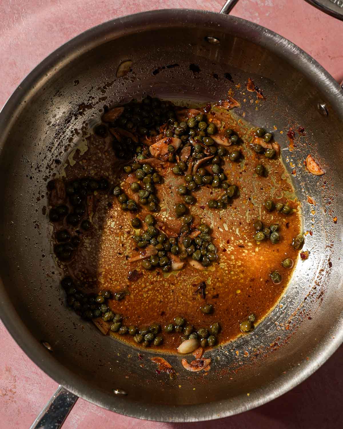 A pan with capers, garlic, and oil simmering, creating a flavorful sauce base.