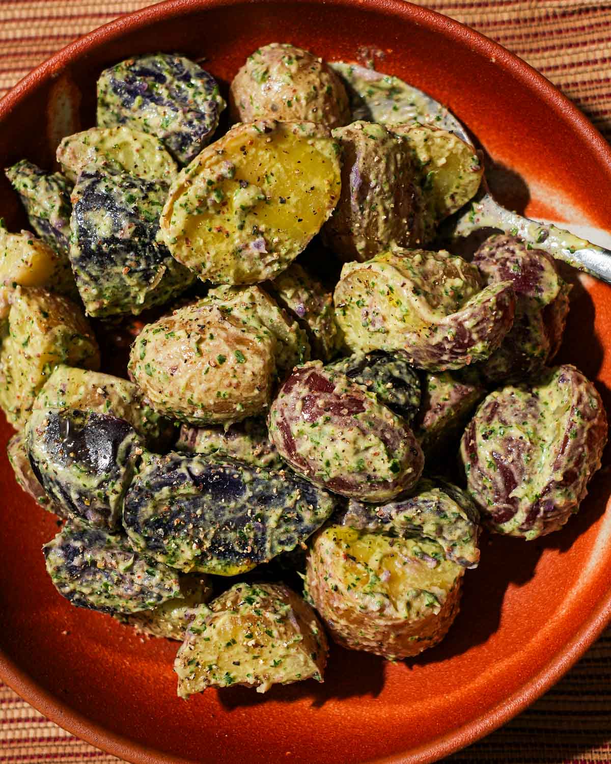 A bowl filled with potato salad with Chimichurri mayo with a spoon in it.