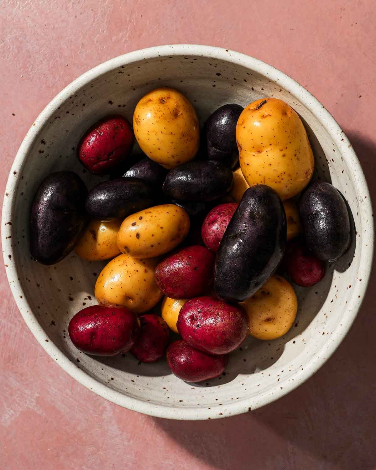 A bowl of red, white, and blue small potatoes on a pink table.
