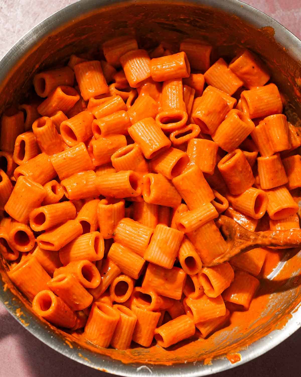 A large skillet of pasta tossed with roasted red pepper and tomato pasta sauce.
