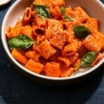 A large shallow bowl of roasted red pepper and tomato pasta with basil and parmesan cheese.