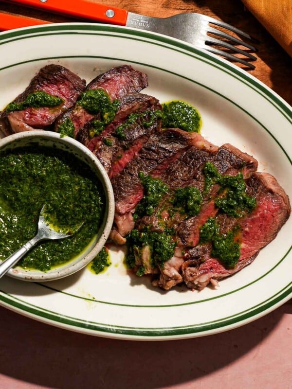 A plate of sliced ribeye steak with caper chimichurri sauce in a small bowl with a spoon.