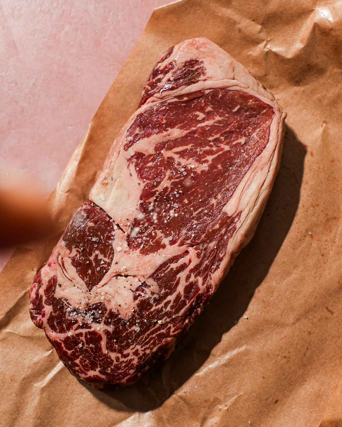 Raw ribeye steak with salt on top of brown parchment paper.