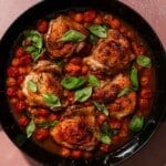 A pan of cooked chicken thighs with cherry tomatoes and basil.