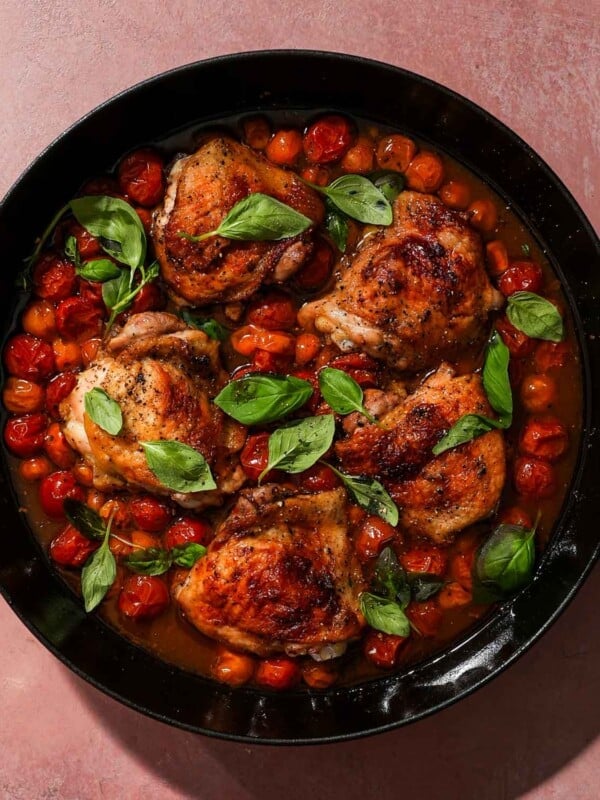 A pan of cooked chicken thighs with cherry tomatoes and basil.