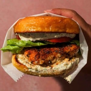 Hand holding a blackened fish sandwich with lettuce, tomato, and tartar sauce.