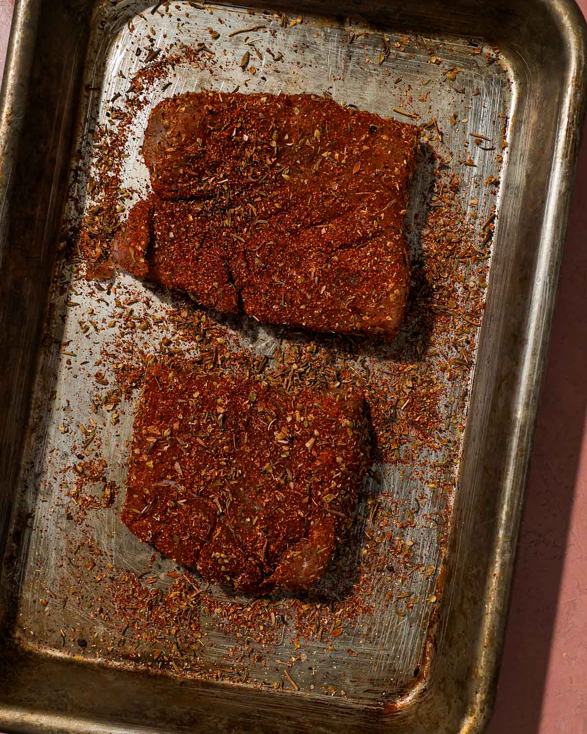 Two seasoned fish fillets coated in blackening spices on a metal tray.