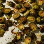 Roasted Brussels sprouts with chili flakes and honey glaze scattered on parchment.